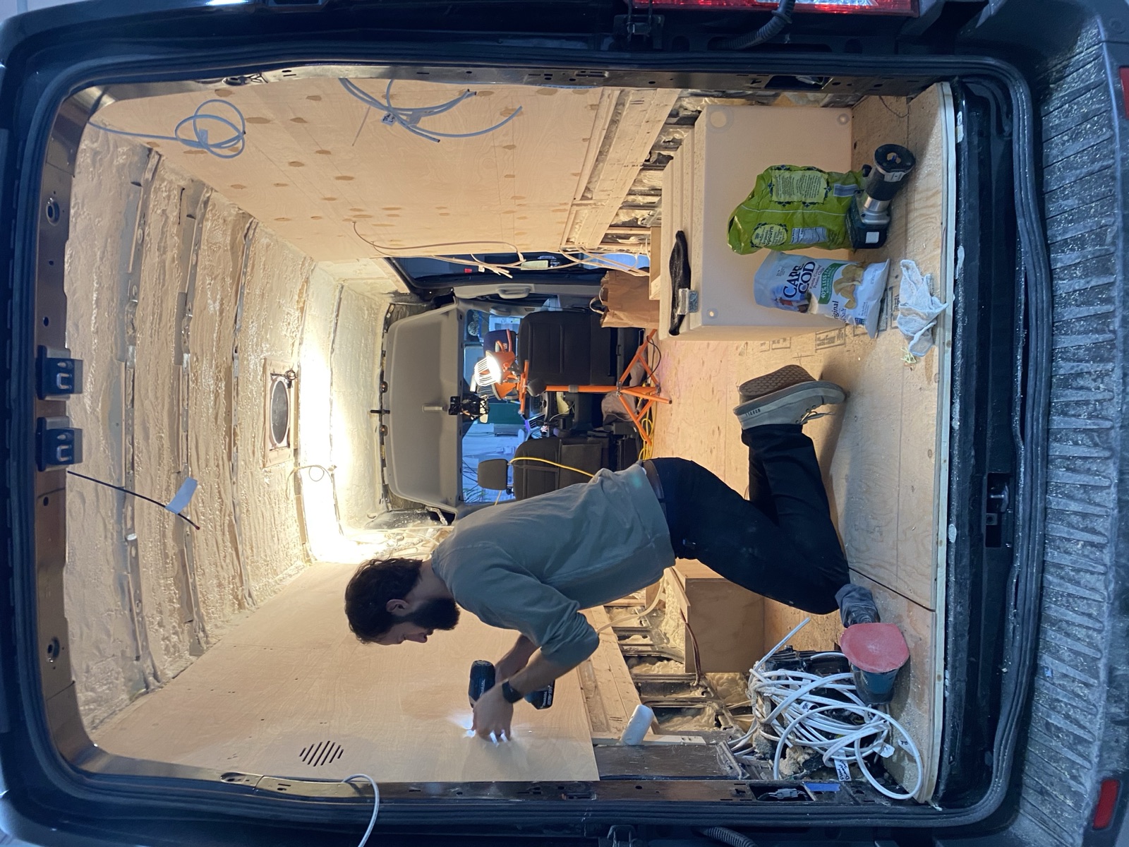 Mark kneeling inside the van, drilling into the wall panels