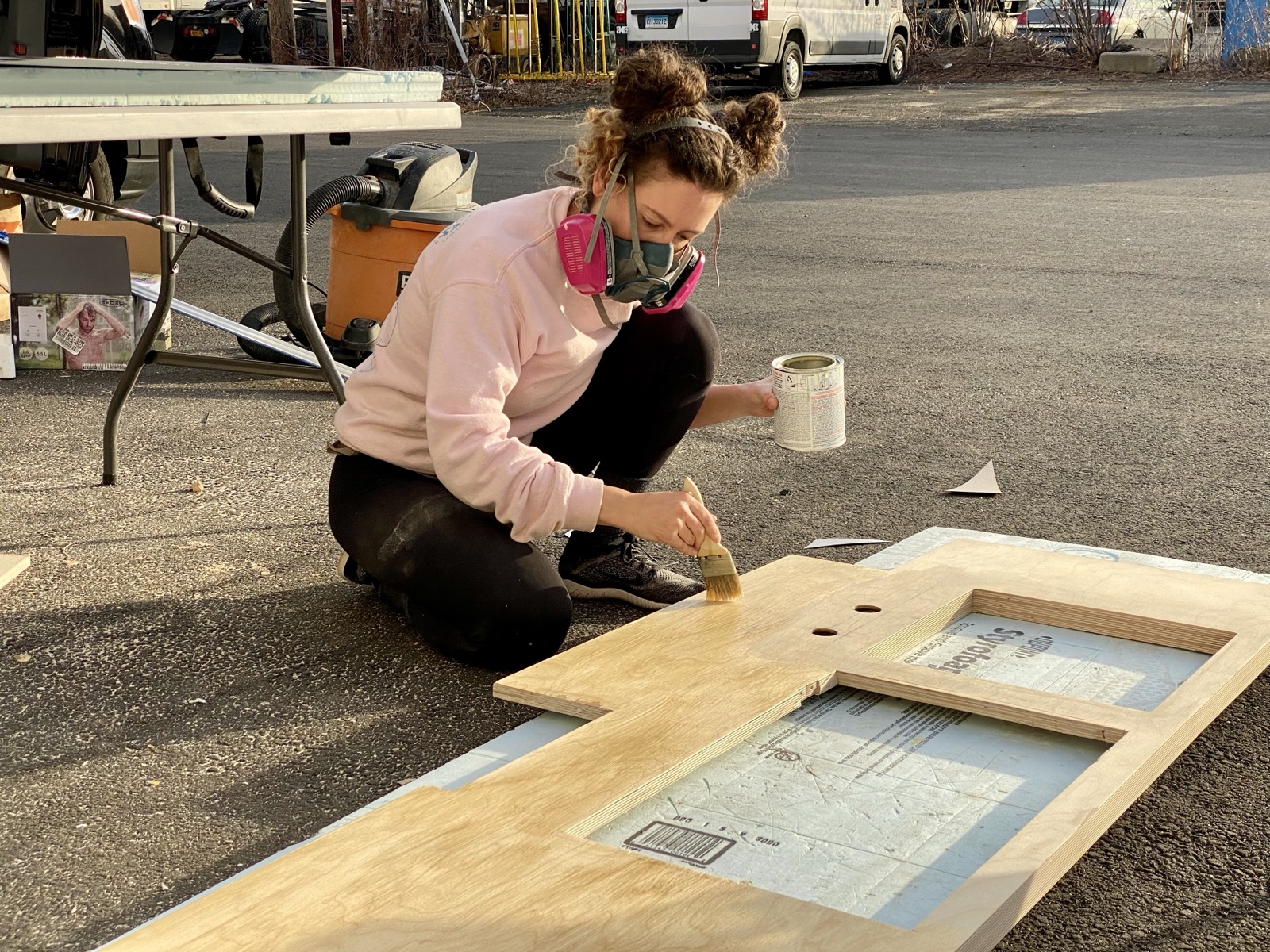 Cristina in a respirator, brushing finish onto a plywood panel outdoors