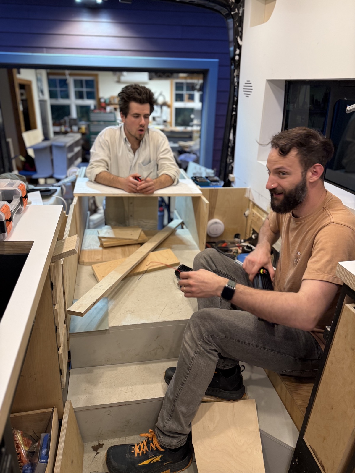 Two people building the new day-bed base inside the van